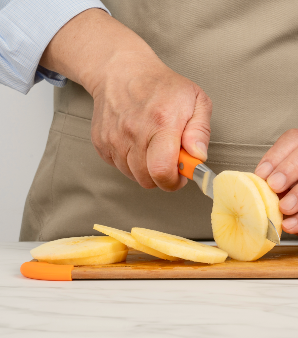 Person slicing apples with a knife on a wooden cutting board.