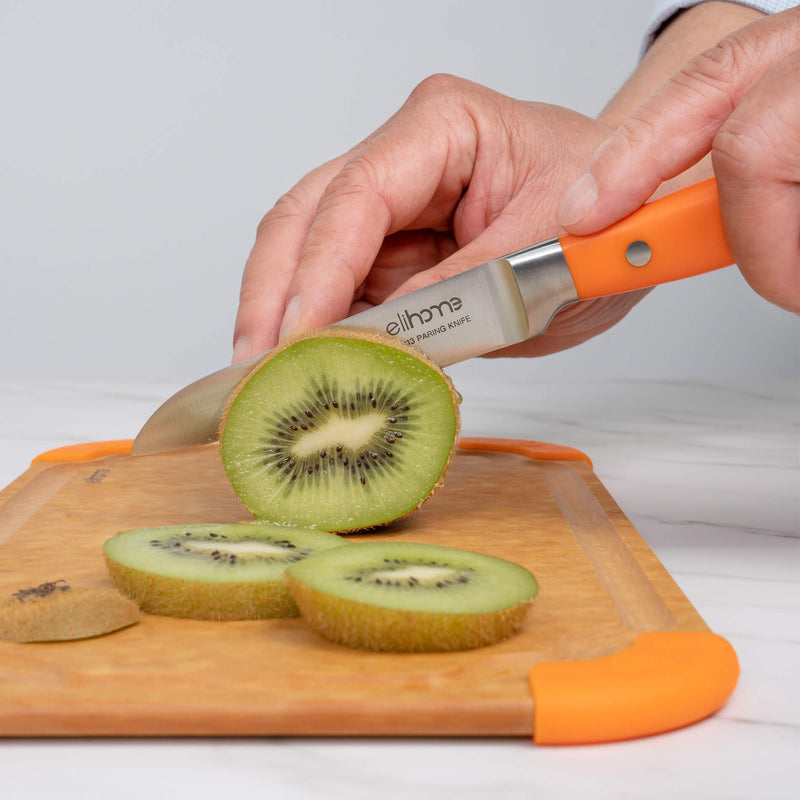 Hands slicing fresh kiwi with Elihome paring knife with orange handle on wood fiber cutting board with orange silicone corners