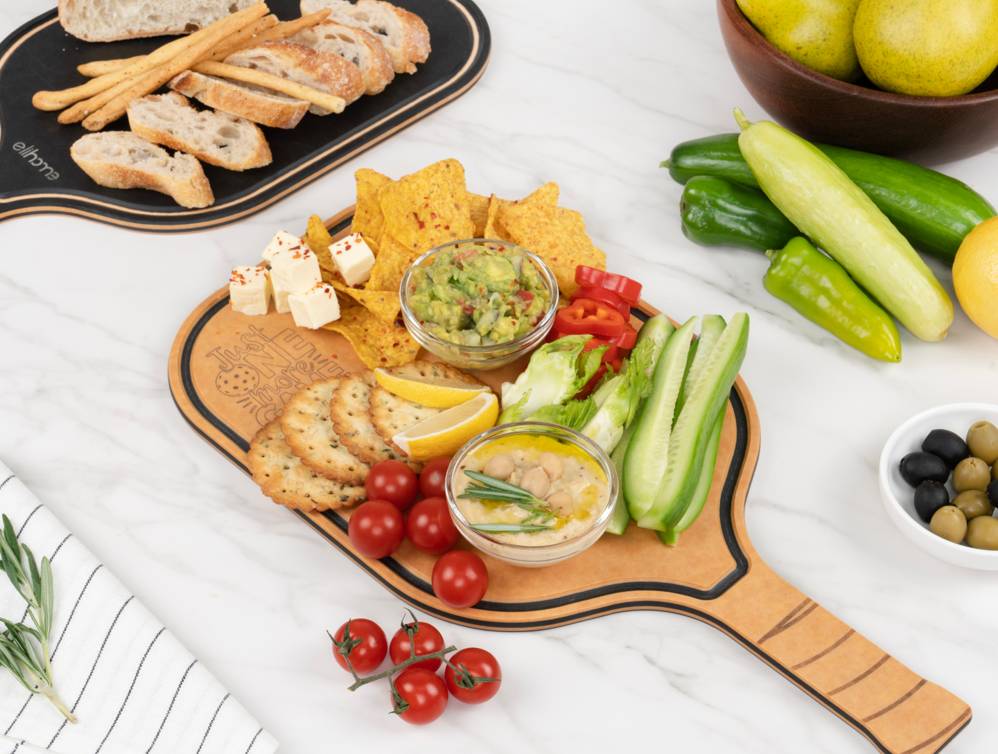 Elihome pickleball-shaped charcuterie cutting board styled with crackers, guacamole, hummus, fresh vegetables, and cheese