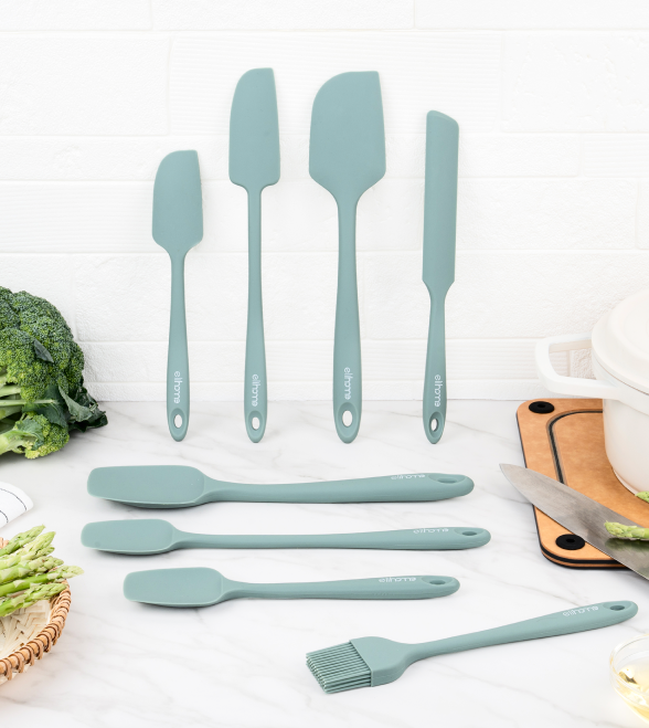 Set of light blue silicone kitchen utensils on a white surface with vegetables and a cutting board.