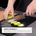 Close-up of a chef's knife slicing zucchini on an Elihome black wood fiber cutting board, demonstrating the surface quality. Text reads: "Knife Friendly. Resist deep cut marks and protect your knives."