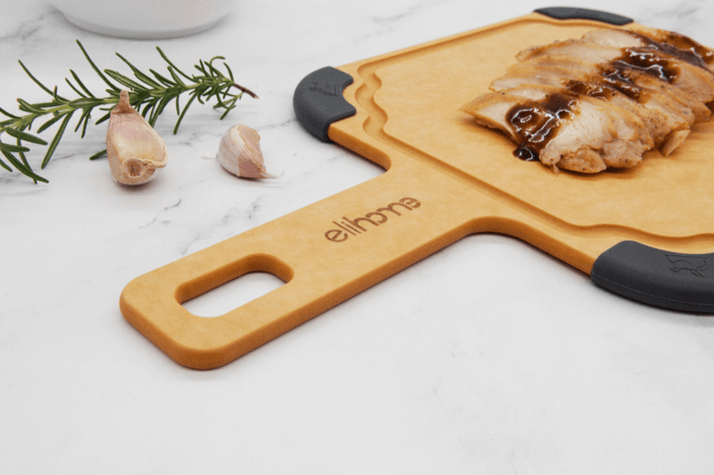 Elihome wood fiber cutting board with handle and gray silicone corners, displaying sliced grilled chicken with teriyaki sauce, garlic and rosemary