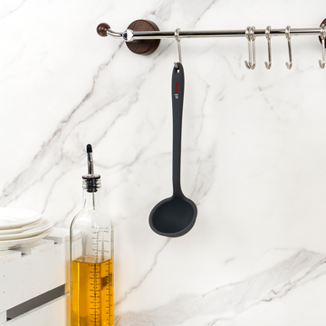 Elihome Classic Ladle in Gray hanging from a kitchen rail beside a glass oil bottle and stacked plates on a marble wall