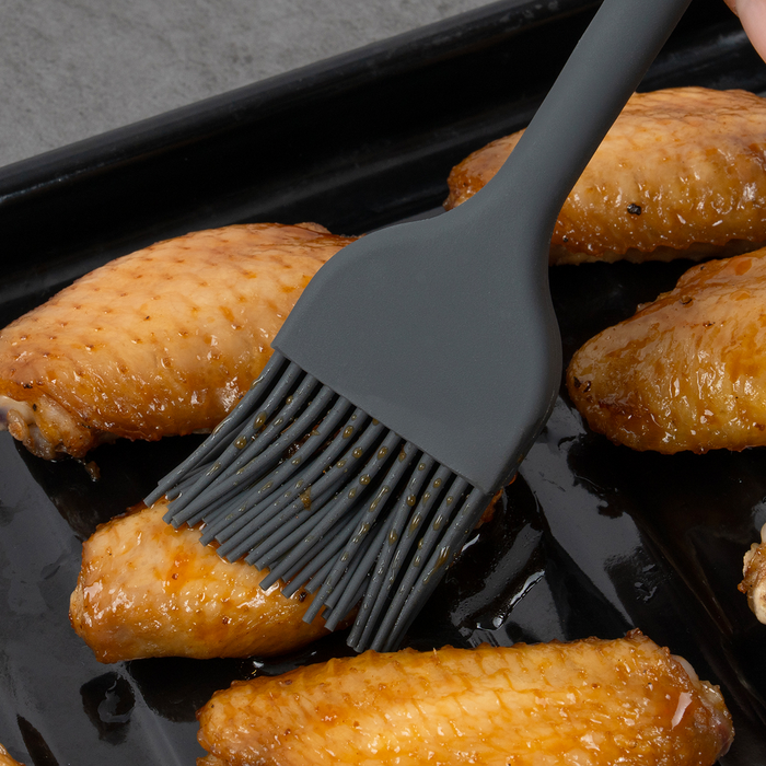 Elihome Mini Basting Pastry Brush from the silicone kitchen tool set in use, glazing baked chicken wings on a sheet pan