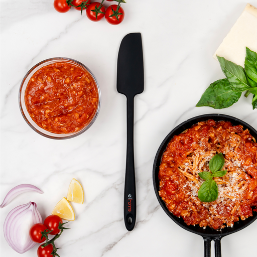 Elihome Skinny Slim silicone spatula in Black on a marble counter between a jar of tomato sauce and a skillet of pasta with basil and parmesan