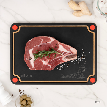 Black side of the Elihome x Peanuts 4-in-1 cutting board with a raw tomahawk steak, rosemary and peppercorns, red corner feet for raw meat