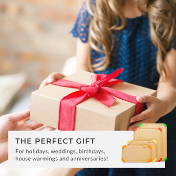 A person holding a gift box with a red ribbon, presenting the cutting board set as the perfect gift for holidays, weddings, birthdays, housewarmings, and anniversaries.
